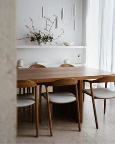 a dining room table and chairs in front of a wall with flowers on the shelf