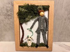 an image of a doll in a frame with moss on the ground and a small owl sitting next to it