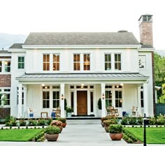 a large white house with lots of windows and plants in the front yard, on a cloudy day