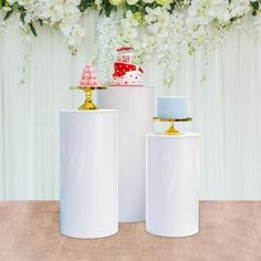 three white vases with cakes on them and flowers in the background