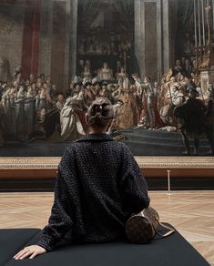 a woman sitting on a cushion in front of a painting that is being displayed at the museum