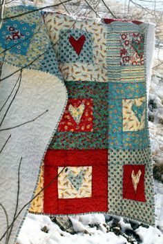 a patchwork quilt hanging from a tree branch in the snow with hearts on it