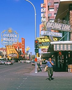 a man is walking down the street in front of some neon signs and buildings on a sunny day