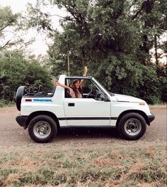 two people in the back of a white car waving and sitting in the driver's seat