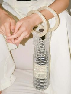 a woman is holding a wine bottle in her hand while sitting on a white chair