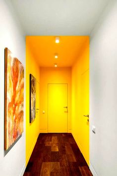 an empty hallway with yellow walls and wood flooring is pictured in this image, there are two paintings hanging on the wall