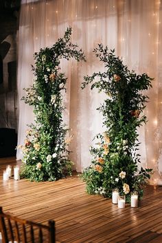 an arrangement of greenery and candles on a wooden floor in front of a curtain