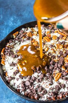 someone pouring caramel sauce on top of chocolate chips in a skillet filled with oatmeal