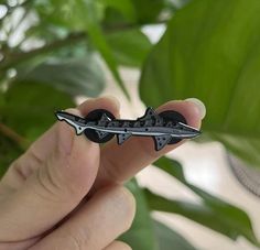 a person holding a small metal object in their left hand and green plant behind it