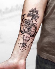 a man with a tattoo on his arm holding a compass and bull skull in the middle