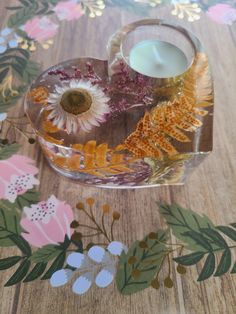 a glass candle holder sitting on top of a wooden table covered in flowers and leaves