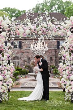 a bride and groom kissing under an archway decorated with pink flowers in front of a house