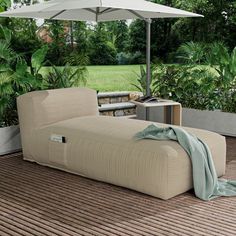 an outdoor lounge chair and umbrella on a deck with trees in the backgroud