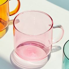 three different colored glass mugs sitting next to each other on a white counter top