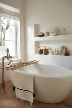 a white bath tub sitting in a bathroom next to a window with shelves on the wall