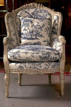 an old chair with blue and white fabric on it's back legs, sitting in a room