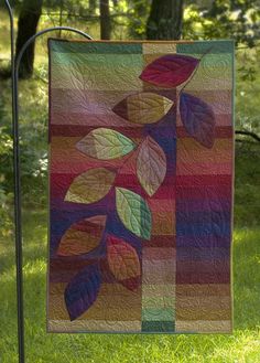 a colorful quilt hanging on a clothes line in the grass with trees in the background