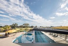 an empty swimming pool with tables and umbrellas on the side, under a partly cloudy blue sky