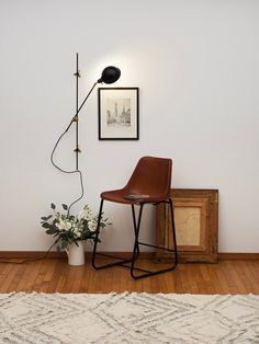 a brown chair sitting next to a white flower vase on top of a hard wood floor