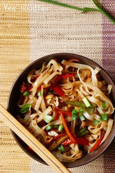 a bowl filled with noodles and vegetables next to chopsticks on top of a table