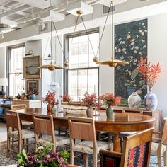 a large dining room table surrounded by chairs and vases with flowers on them in front of windows