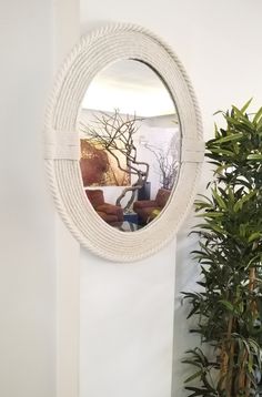 a round white rope mirror hanging on the wall next to a potted plant