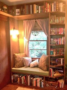 a window seat in front of a bookshelf filled with lots of books and pillows