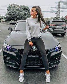 a woman sitting on the hood of a bmw car in a parking lot with other cars