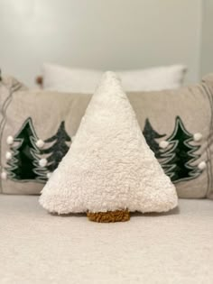 a small white christmas tree sitting on top of a bed next to two pillow cases