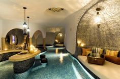 an indoor swimming pool with lights on the ceiling and water running through it, surrounded by stone walls