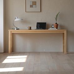 a wooden table with a laptop on it in front of a wall mounted clock and potted plant