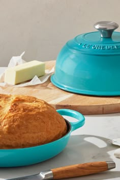 a loaf of bread sitting in a blue casserole on top of a wooden cutting board