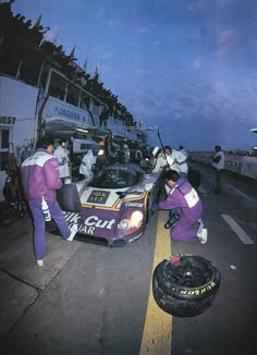 two men working on a race car in front of the pit area at night time