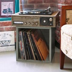 a record player sitting on top of a wooden table next to a chair and wall