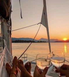 two people sitting on a hammock with wine glasses in their hands at sunset