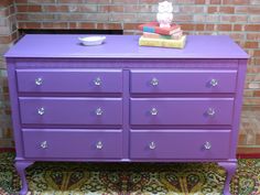 a purple dresser sitting on top of a rug next to a brick wall