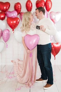 a man and woman standing next to each other with heart shaped balloons in front of them