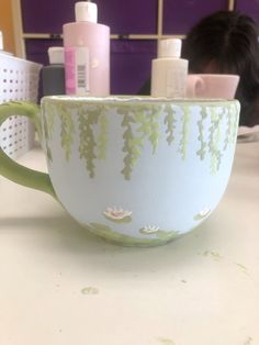 a green and white coffee cup sitting on top of a table next to a person