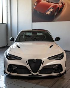 the front end of a white sports car in a showroom with a painting on the wall