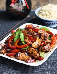 a white plate topped with chicken and veggies next to two bowls of rice