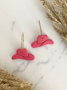 two pink heart shaped earrings sitting on top of a white table next to dried grass