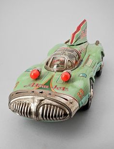 a green toy car with red eyes on it's head and nose, sitting on a gray surface