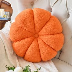 an orange round pillow sitting on top of a white chair next to flowers and a vase