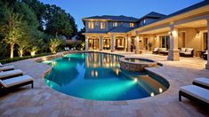 an outdoor swimming pool surrounded by lounge chairs and trees at night with lights on it