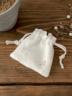 a white bag sitting on top of a wooden table next to a necklace and a bowl