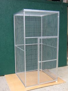 a large bird cage sitting on top of a piece of wood next to a green wall