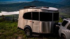 an rv parked on top of a lush green hillside next to a white pickup truck