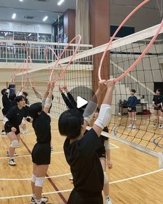 some girls are playing volleyball on a court with their hands in the air and one girl is reaching up to hit the ball