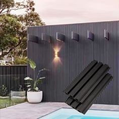 an outdoor swimming pool with black tiles and lights on the wall next to it in front of a house