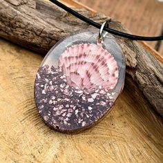 a pink shell on a black cord is sitting on a piece of wood with a wooden stick